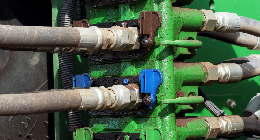 Mangueiras e conexões hidráulicas acopladas a bloco metálico verde com válvulas de controle.