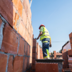 Trabalhador da construção civil levantando parede de tijolos em estrutura de obra.